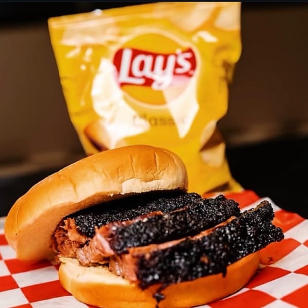 Fat Floyd's Barbecue brisket sandwich on a bun with a bag of Lay's chips in the background.