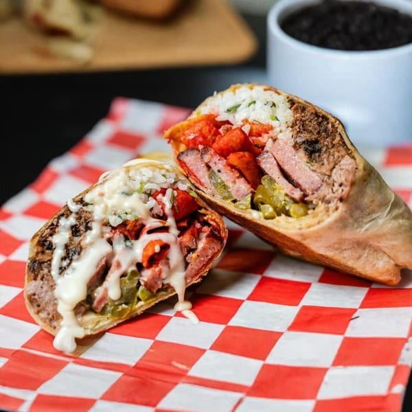 Two halves of a Fat Floyd's barbecue burrito, filled with meat, rice, and sauce, on checkered paper.