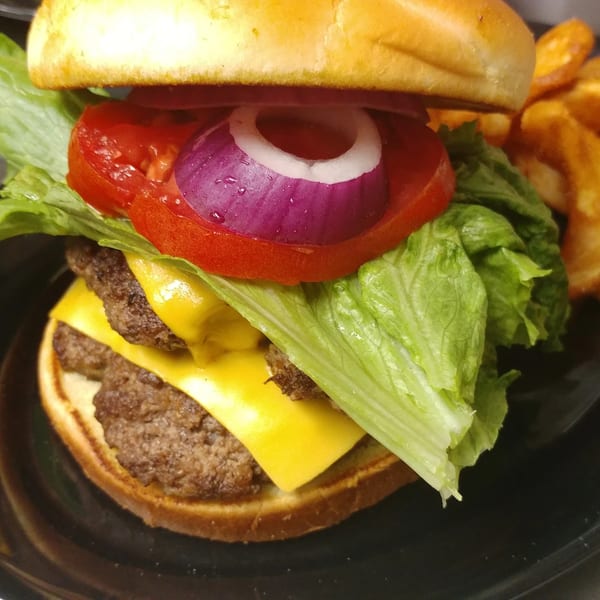 A double cheeseburger with lettuce, tomato, and red onion, served with a side of fries.