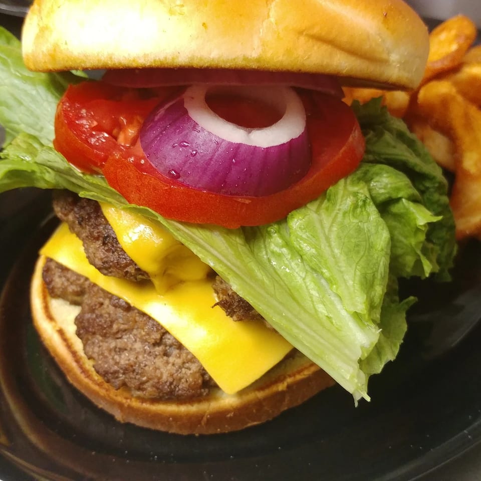 A double cheeseburger with lettuce, tomato, and red onion, served with a side of fries.