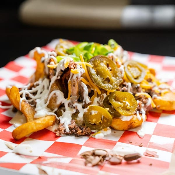 Fat Floyd's loaded fries with pulled pork, cheese, jalapenos, and white sauce on checkered paper.