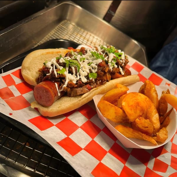 A Fat Floyd's Barbecue hot dog topped with chili, white sauce, and cilantro, served with fries.